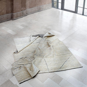 Fields Natural Landscape Rug draped and slightly ruffled over a white stone floor and a few steps - by Rezas