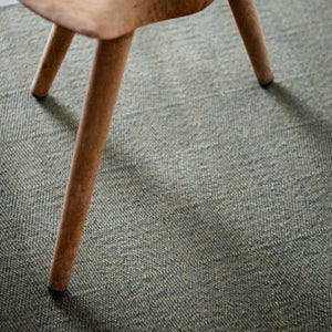 A close up of Fabula Living’s Forest Rune Rug, with a wooden stool sat on top of the textured forest green rug - by Jens Landberg Schrøder