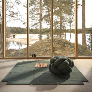 Living room with Design House Stockholm wool green Basket rug in the centre, and a view of a natural landscape through the windows