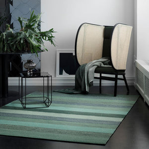 Fabula Living’s Green Veronica Rug sat on a dark wood floor with a side table, plant and chair sat on the far side of the rug. 