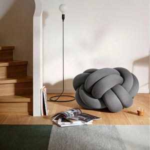 Design House Stockholm Green/Grey Fields Rug, by Lena Bergström, placed on an oak floor next to a floor cushion, lamp and a few magazines scattered nearby..