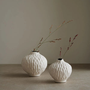Two of Lindform’s Line sand cut vases finished in a natural colour and a sculpted surface pattern, shown placed on a worktop with neutral background 