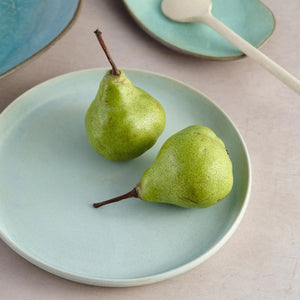 Julie Damhus’ Mint Toto Plate on a table with green pairs and other ceramic plates.
