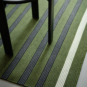 Fabula Living’s Moss/Black Fleur Rug has stripes-within-stripes. The well-balanced pattern is woven in harmonious moss green and black. Close up of rug under black chair.