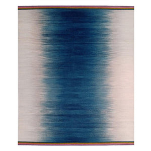 Gelim rug by Ptolemy Mann with a central ikat stripe in an inky petrol blue which transitions into pale grey in a distinctively ombre style feathered pattern.