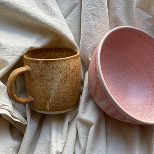 Julie Damhus’ Rose pink speckled colour glazed Oda bowl with brown ceramic mug on linen tablecloth..