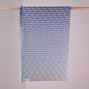 Arra Textiles Smoke Fleet Blanket is woven in soft, lightweight merino wool. This pale blue blanket has hints of aqua and warm neutrals as the colours graduate from light to dark blue. Inspired by the sea.